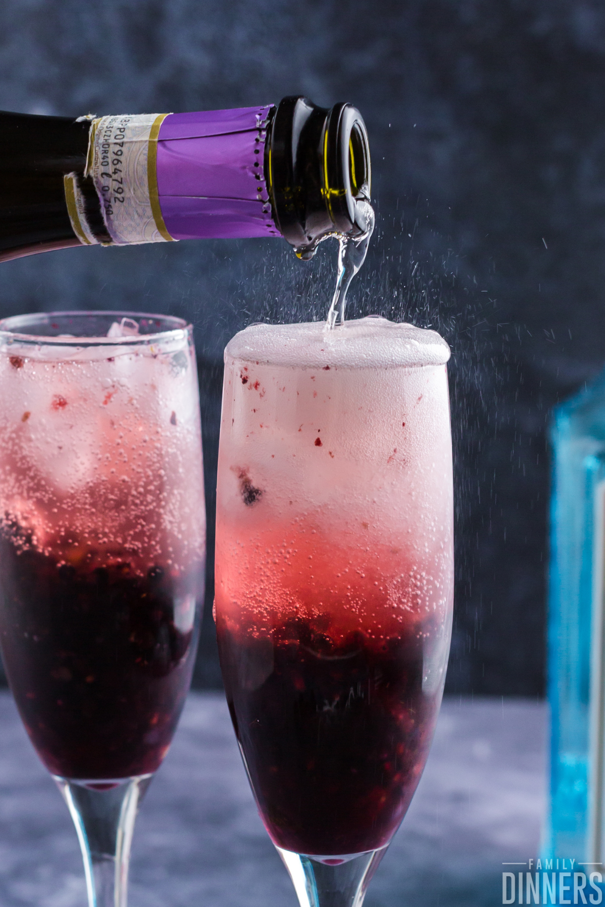 two champagne glasses with blackberry drink inside. Darker blackberry color on the bottom of the glass and light translucent blackberry color at the top. Each glass has fresh thyme and a blackberry on top. Lots of bubbles inside the glass.