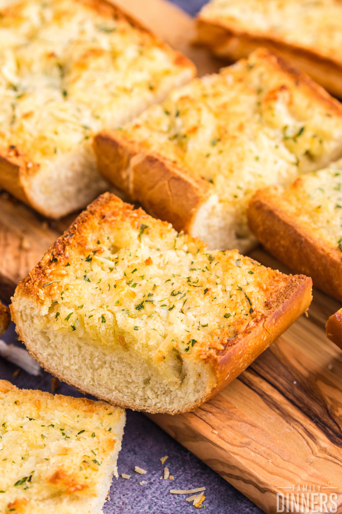 This slices of garlic cheese bread with garlic butter and parmesan cheese on top sitting on a wood cutting board.