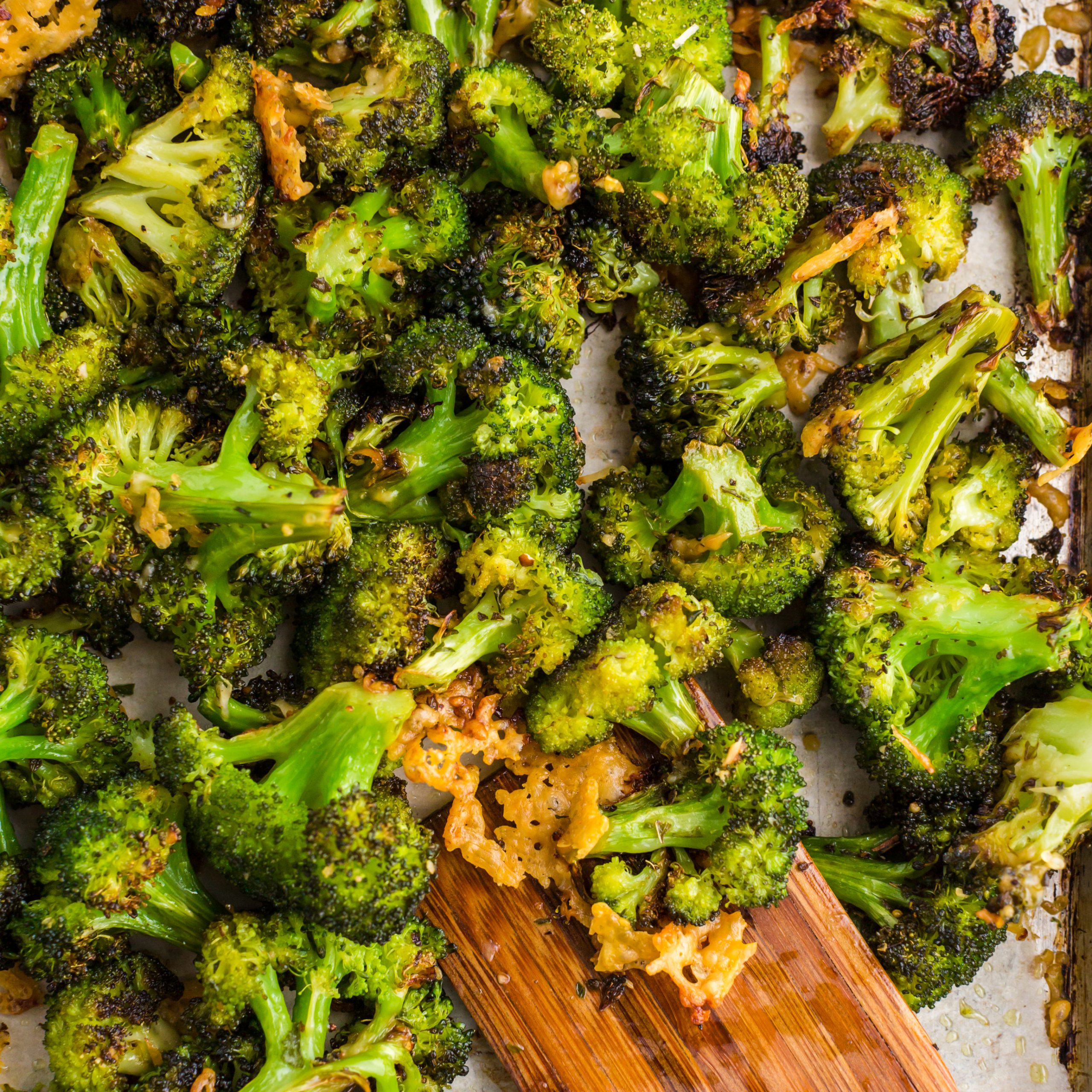 baking sheet with parmesan roasted broccoli on top and wooden spatula