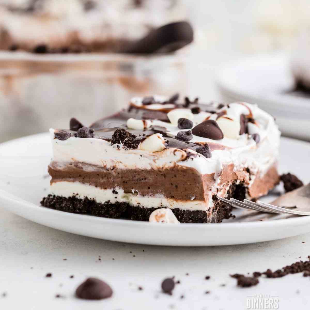 square slice of 4 layer no bake layered chocolate and whipped cream dessert on a white plate.