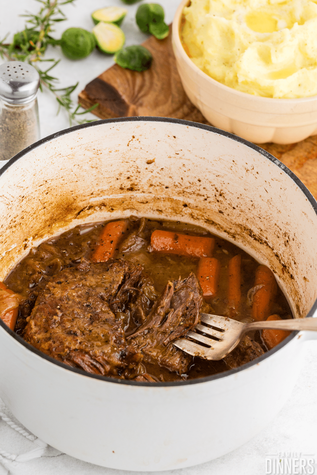 white dutch oven full of pot roast and carrots