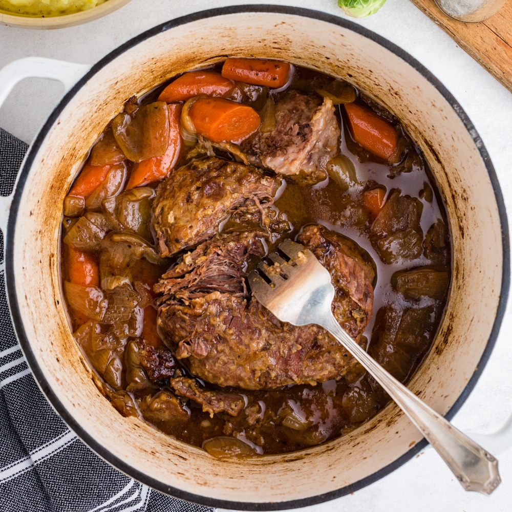 overhead view of cooked pot roast and carrots in white dutch oven