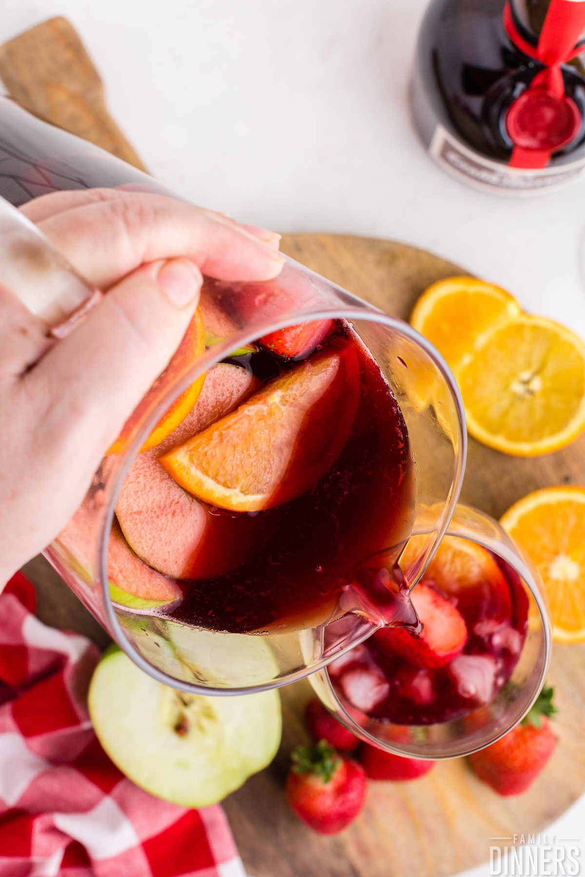 hand holding glass pitcher of red wine sangria with fruit pouring into a glass