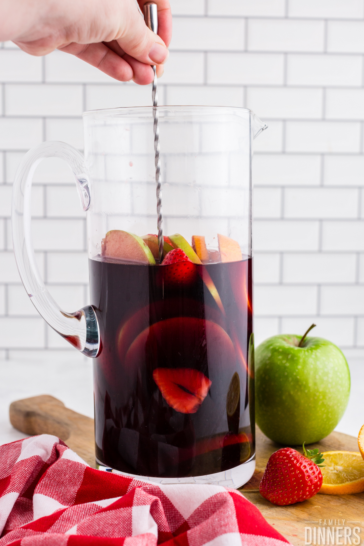 silver stir stick stirring glass pitcher of red wine sangria with fruit inside