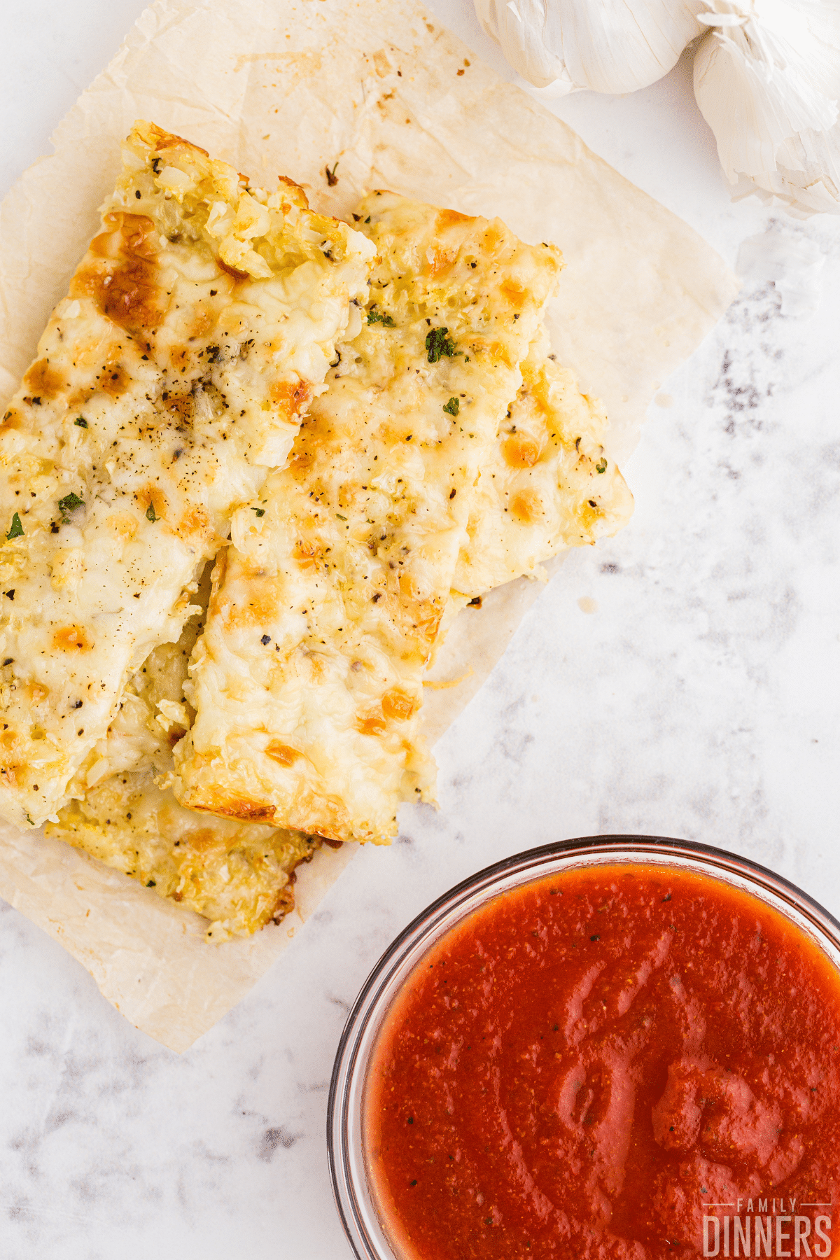 stack of cauliflower breadsticks and bowl of marinara