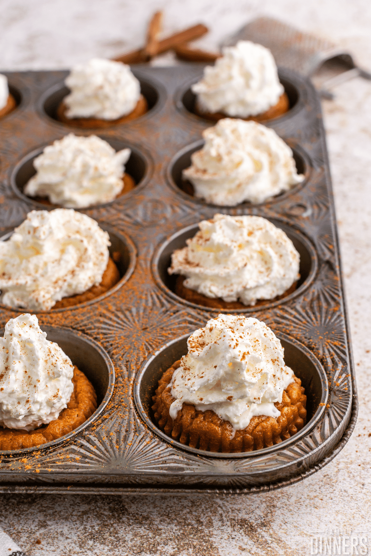 8 mini pumpkin pie cupcake in beautiful decorative cupcake tin. Each little pumpkin pie cupcake is topped with whipped cream and spice.