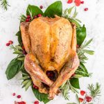 golden roasted turkey on a bed of greens and red cranberries and rosemary and sage