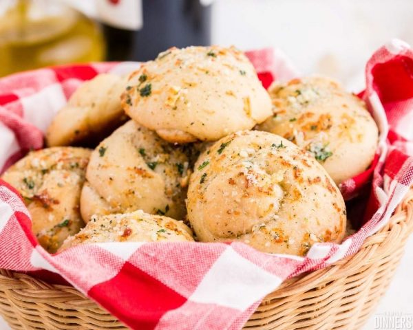 recommended recipe pizza dough garlic knots. Image of wood basket with red and white check plaid cloth inside. Basket is full of seasoned garlic knots