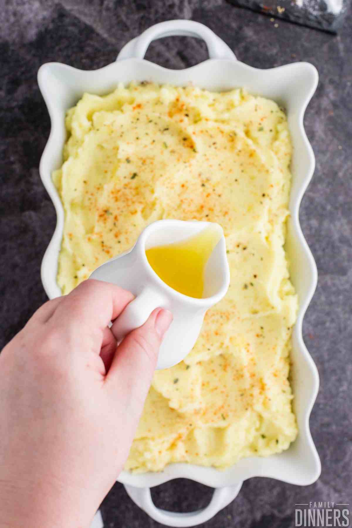 white scalloped dish full of mashed potatoes with butter being poured on top