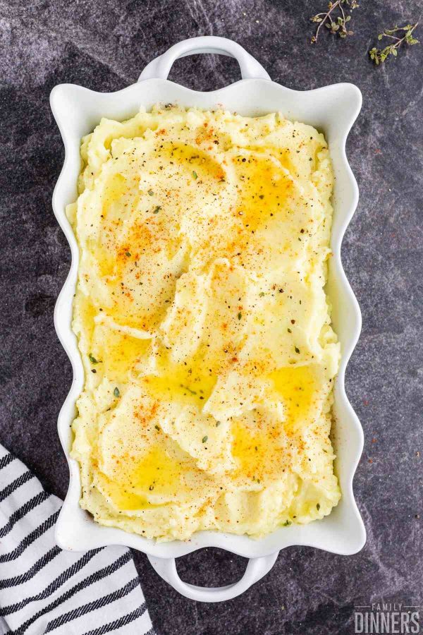 white scalloped dish full of mashed potatoes with butter on top