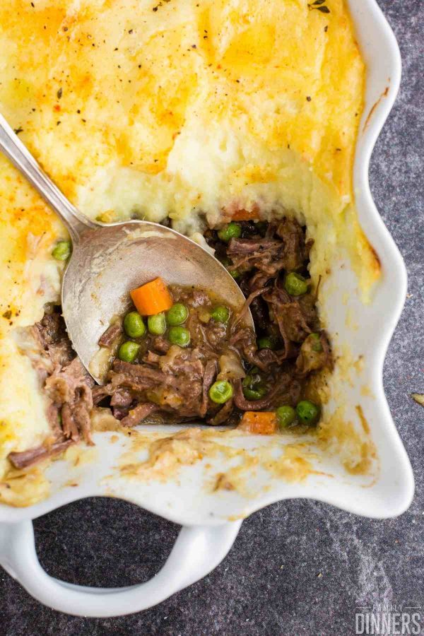large spoon scooping some easy cottage pie out of the casserole dish with shredded beef (pot roast leftovers), peas and corn on the spoon.