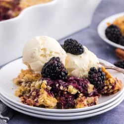 stack of white plates with serving of blackberry dump cake on top of plate with scoop of vanilla ice cream on top