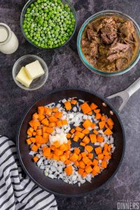 Raw carrots and onions in a black saute pan