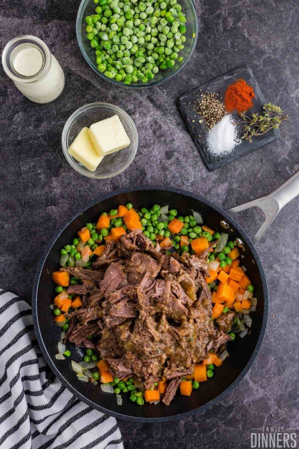 saute pan full of cooked carrots, onions and peas with beef on top