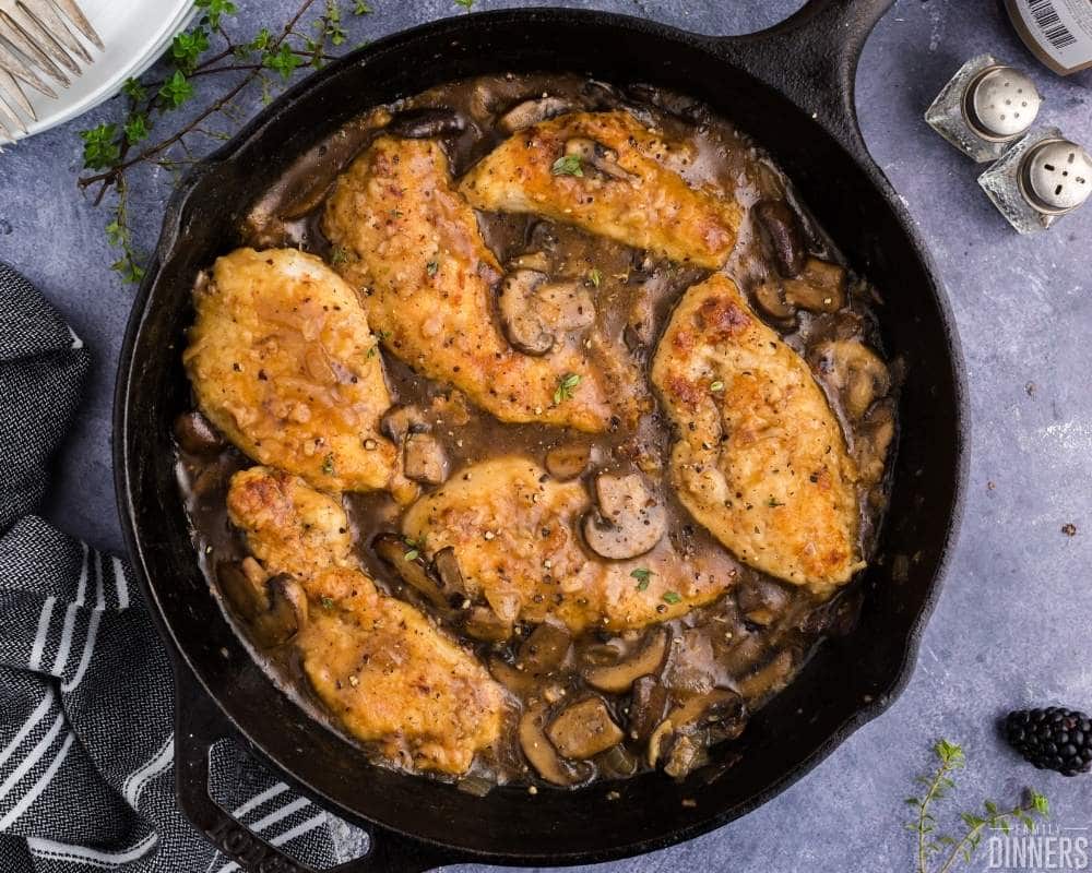 black cast iron pan filled with chicken with a white wine sauce and mushrooms on a blue counter
