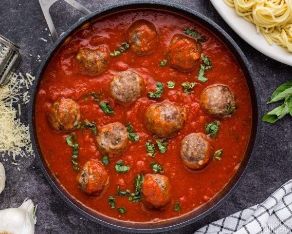 recommended spaghetti and meatballs. Image of dark background with white plate full of spaghetti topped with meatballs, marinara sauce and some parmesan cheese on top