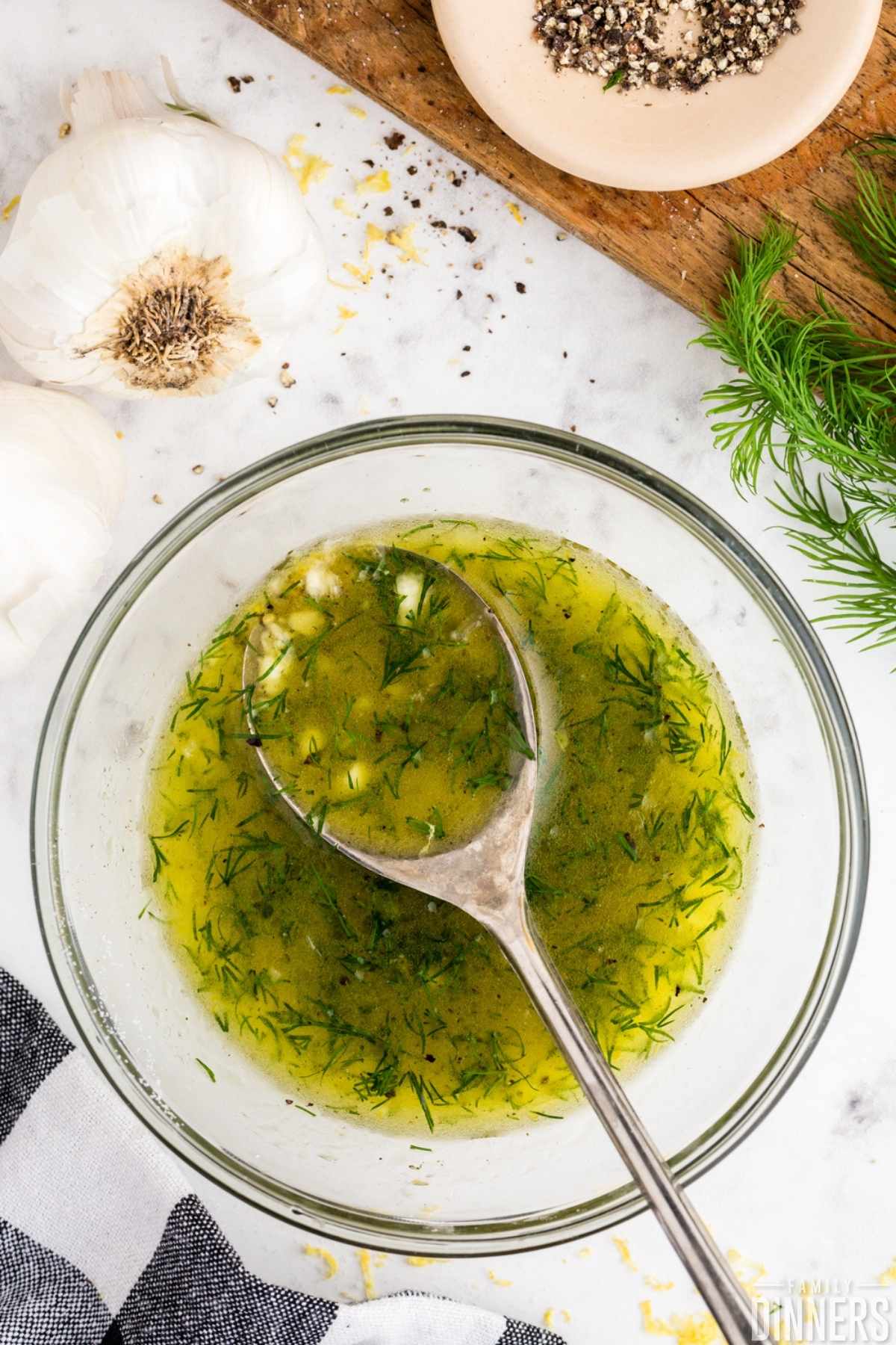 Lemon dill marinade in a clear glass bowl with a large silver spoon ready to spoon lemon vinaigrette on to meat for a salmon marinade or lemon dill chicken marinade.