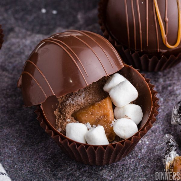 close up of an open chocolate sphere with hot cocoa mix, mini marshmallows, and a chunk of caramel visible inside