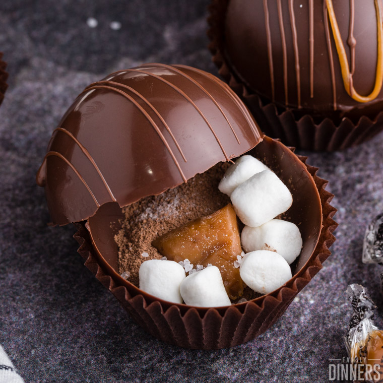 close up of an open chocolate sphere with hot cocoa mix, mini marshmallows, and a chunk of caramel visible inside