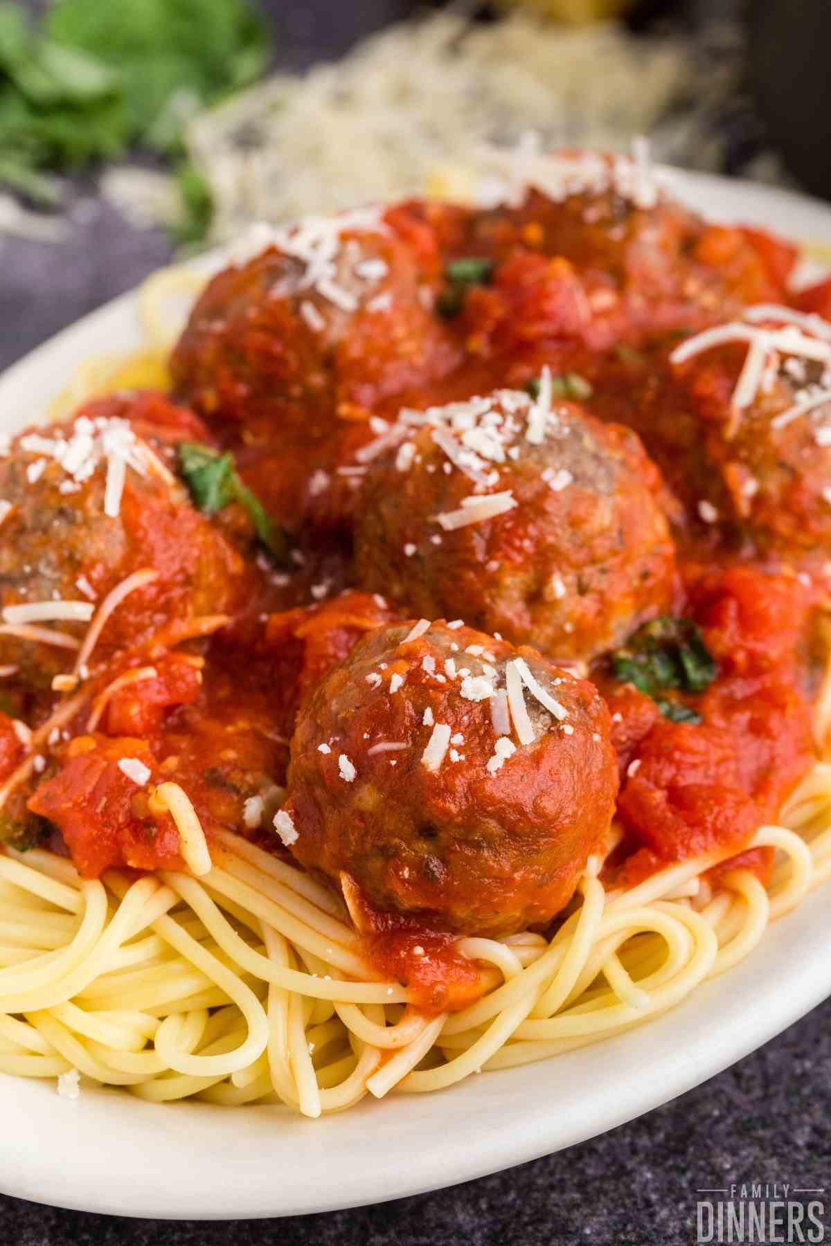 Close up view of a large meatballs with marinara (best spaghetti and meatballs ever) topped with fresh basil and parmesan cheese.