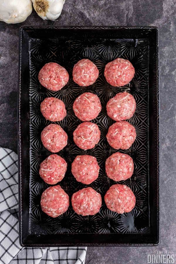 Gray counter. Overhead birds eye view of black decorative baking sheet with 15 uncooked meatballs