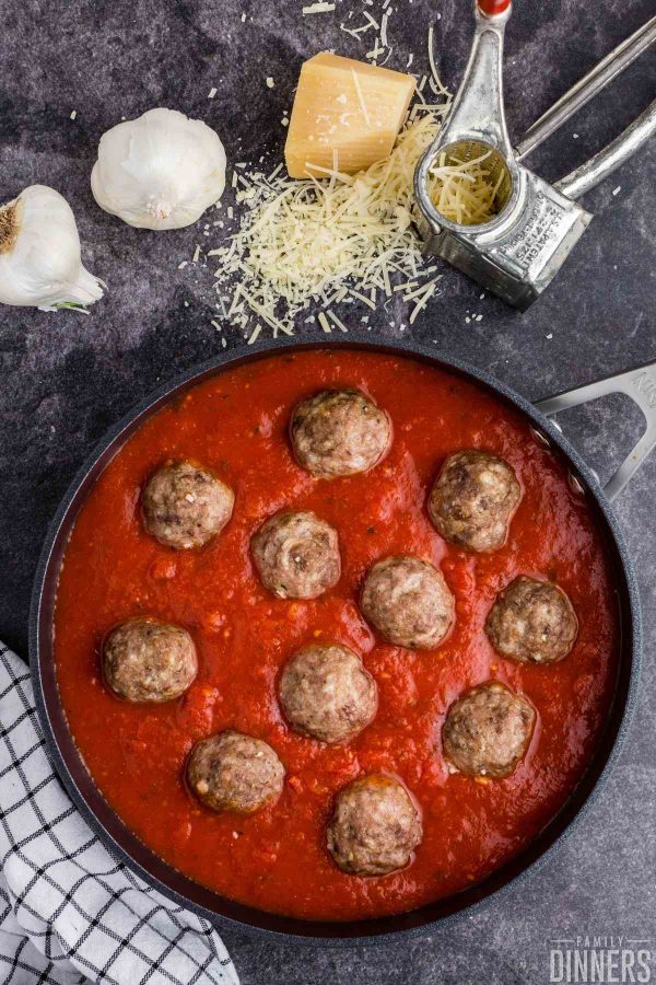 birds eye view of a black large saute pan full of red marinara sauce and 11 large meatballs.