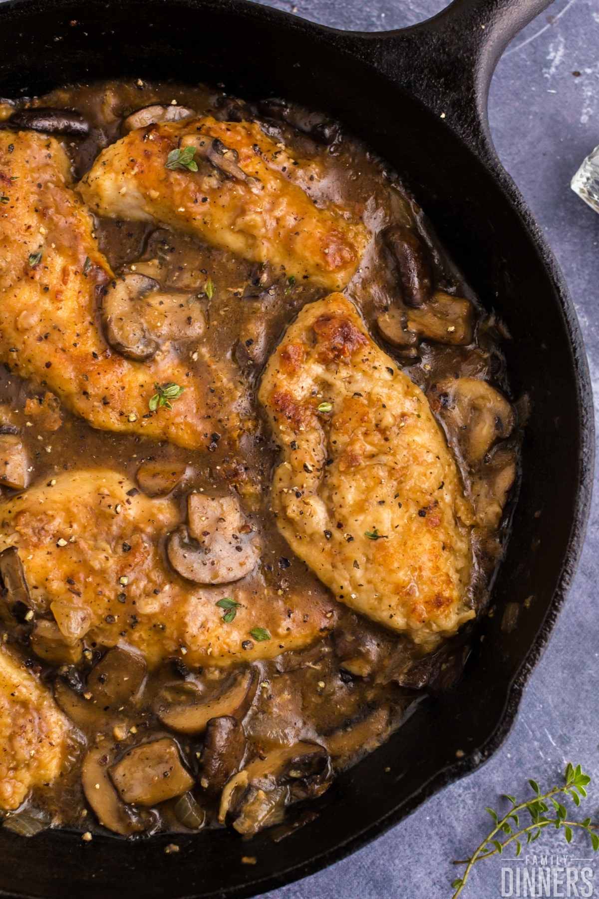 Golden cooked chicken surrounded by mushroom sauce in black cast iron pan.
