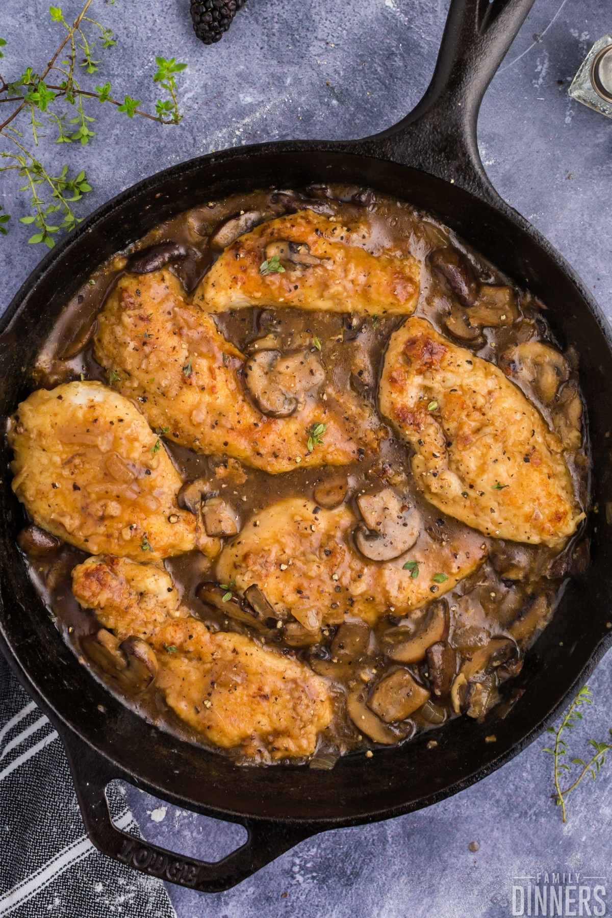 Golden cooked chicken surrounded by mushroom sauce in black cast iron pan.