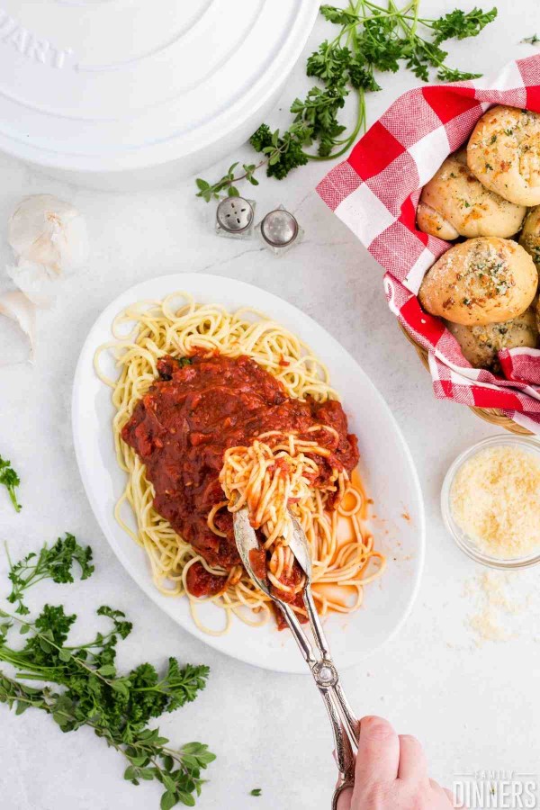 Hand lifting spaghetti with marinara sauce up with tongs.
