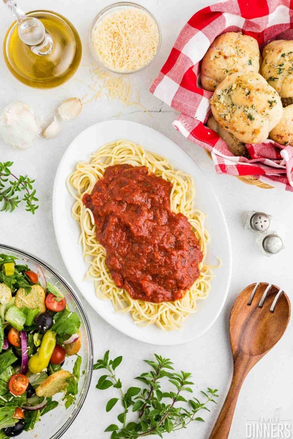 table set with family style spaghetti with spaghetti sauce on top, italian salad and garlic knots.