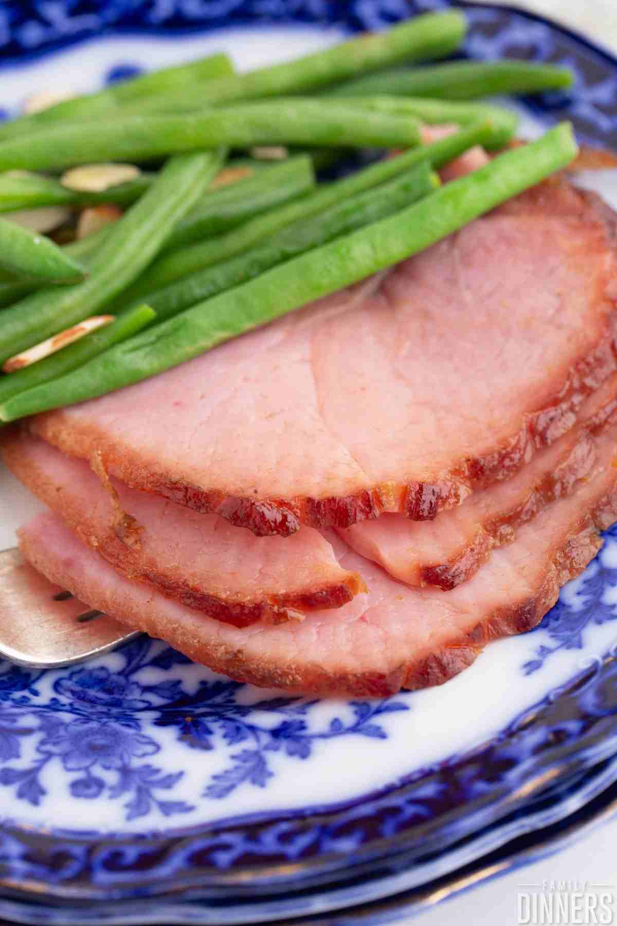Three slices of ham on a plate with green beans and almond slivers.
