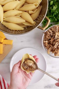 spoon putting carnitas in pasta shell