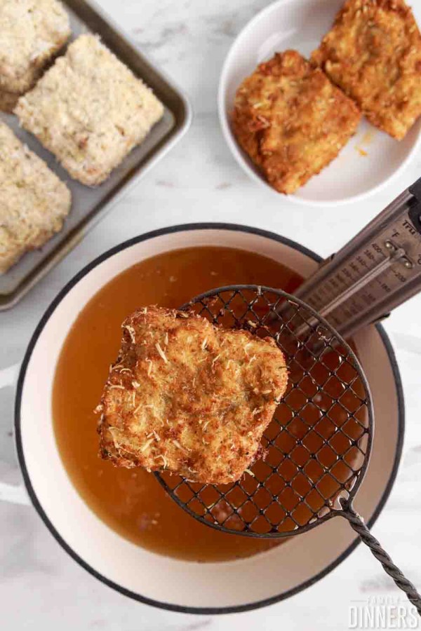 fried, golden brown piece of lasagna on a slotted spoon over cooking oil