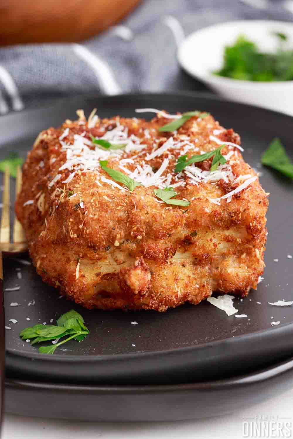 piece of deep fried lasagna on a plate topped with cheese and herbs