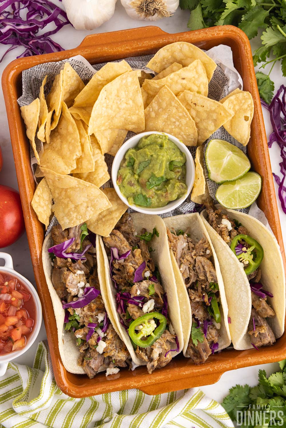 carnitas tacos with chips and guacamole in an orange rectangular dish