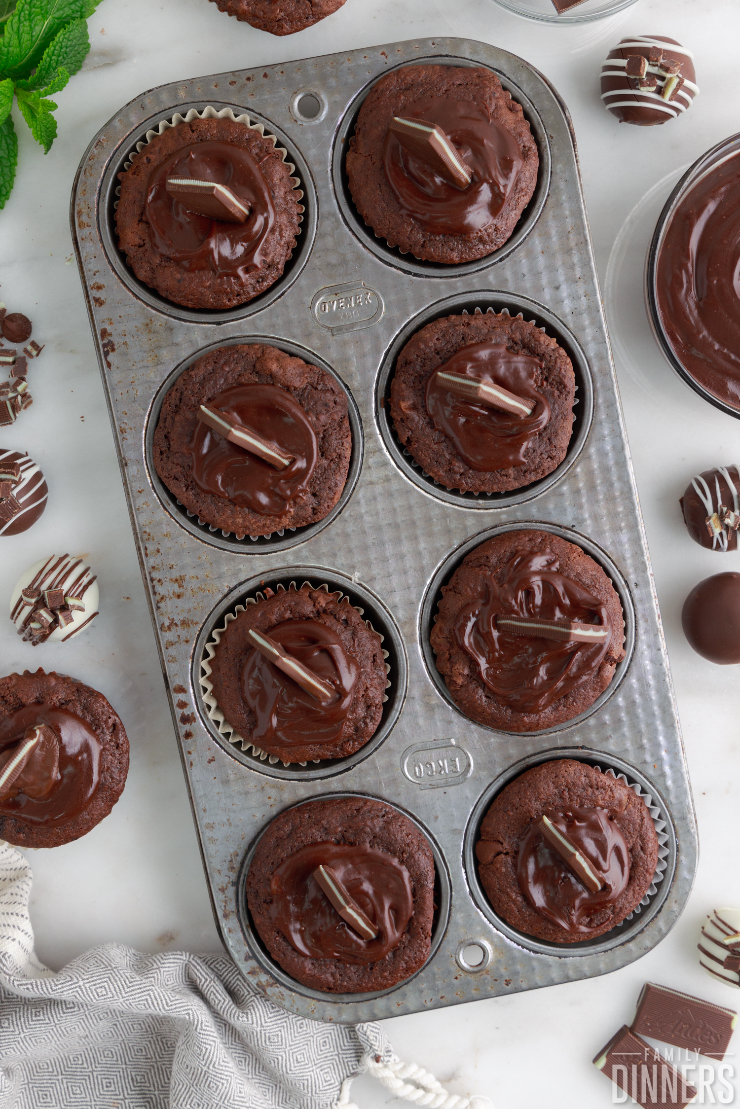 molten mint chocolate muffins in a tin decorated with ganache and Andes mints