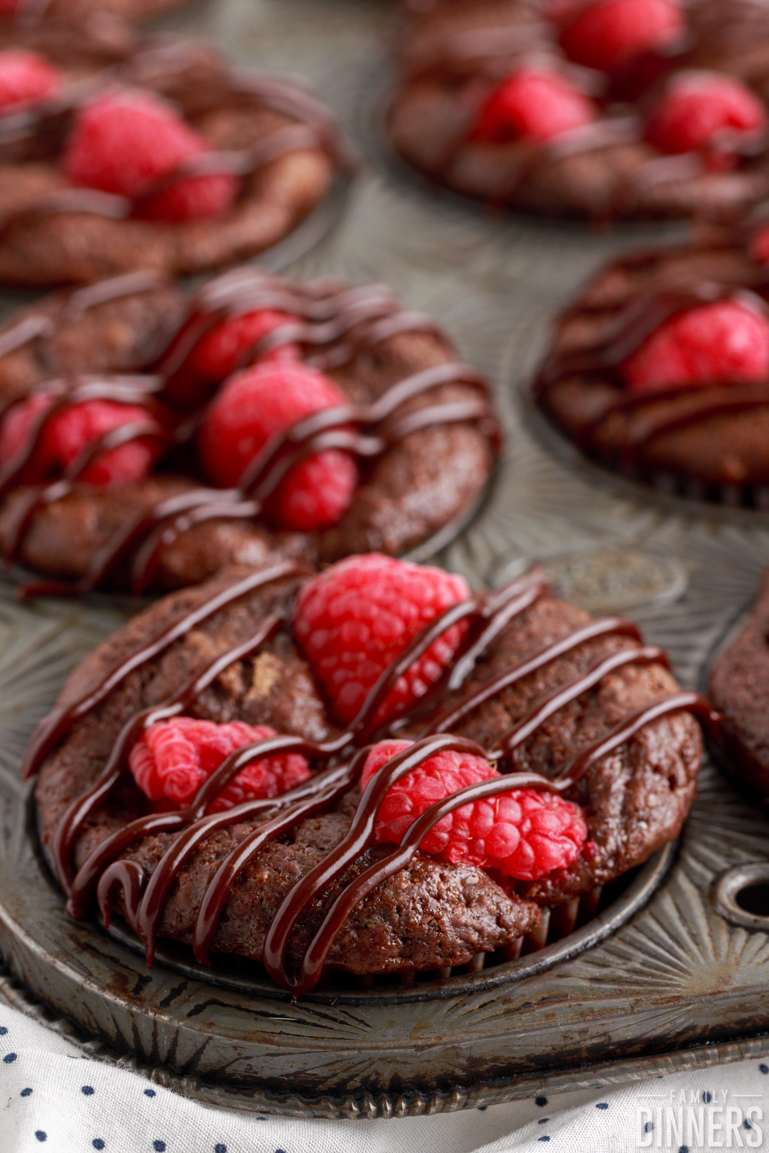 Chocolate muffins in a tin with raspberry and ganache drizzle.