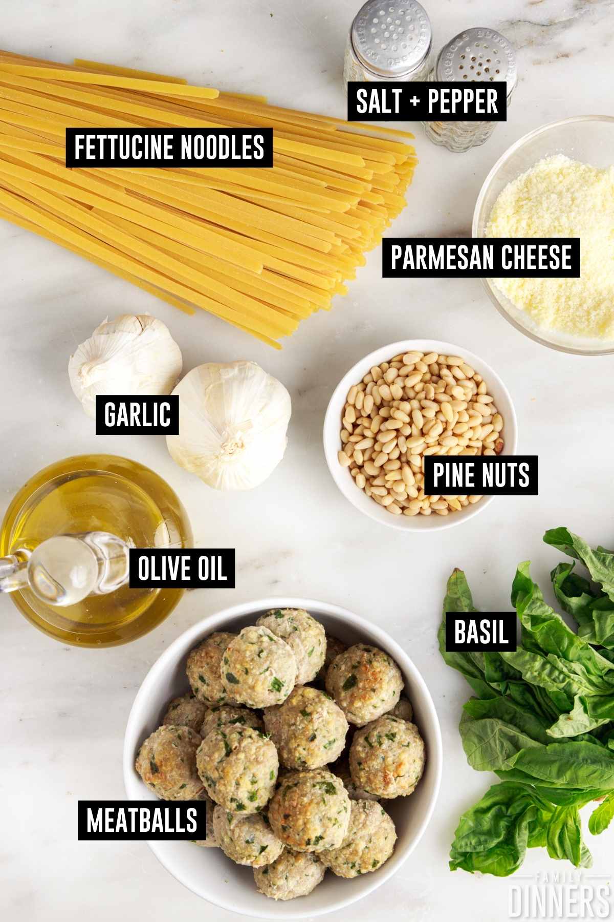 Basil pesto pasta with meatballs ingredients on a counter including: dried fettuccine, garlic, olive oil, parmesan cheese, pine nuts, salt, pepper, basil, garlic and meatballs.