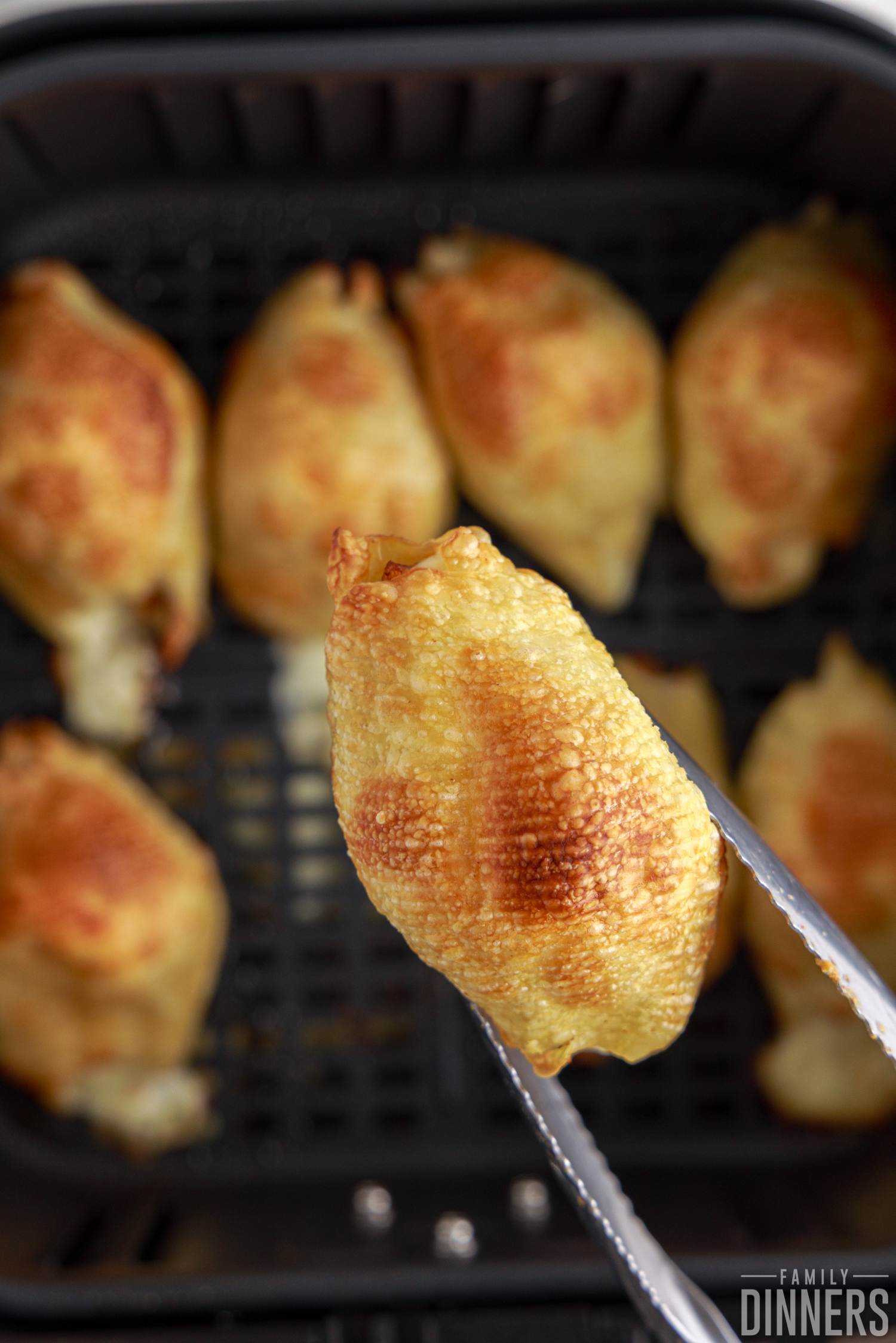 air fried chipotle chicken stuffed shells in the air fryer basket, holding one with a set of tongs