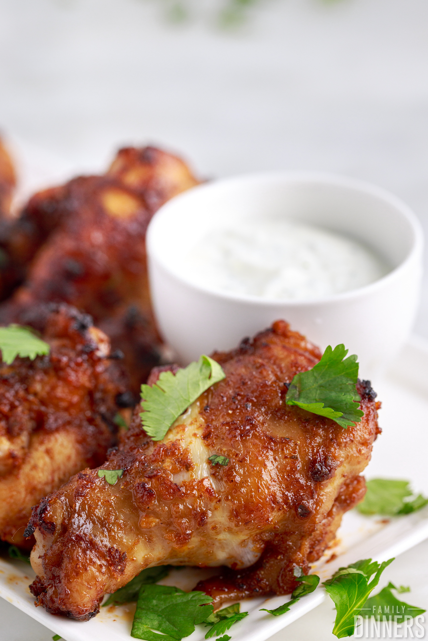 air fried chicken wings and drumettes topped with garnish next to dipping sauce on white plate