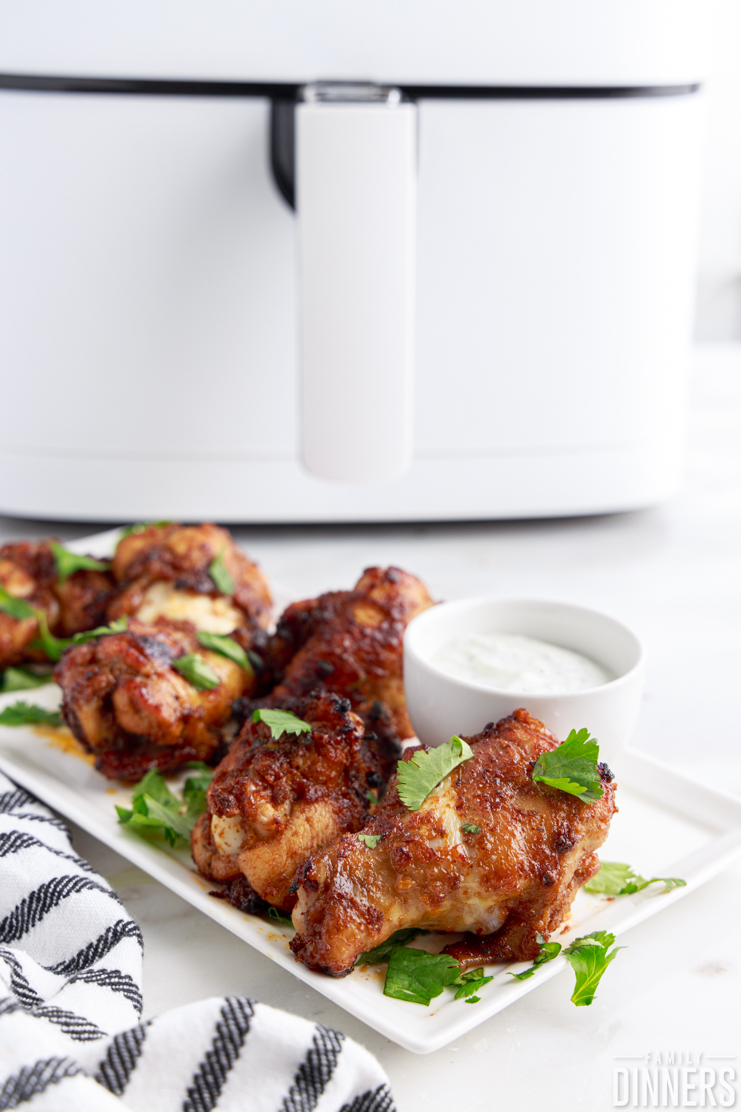 air fryer chipotle chicken wings on a white serving dish with sauce next to white air fryer