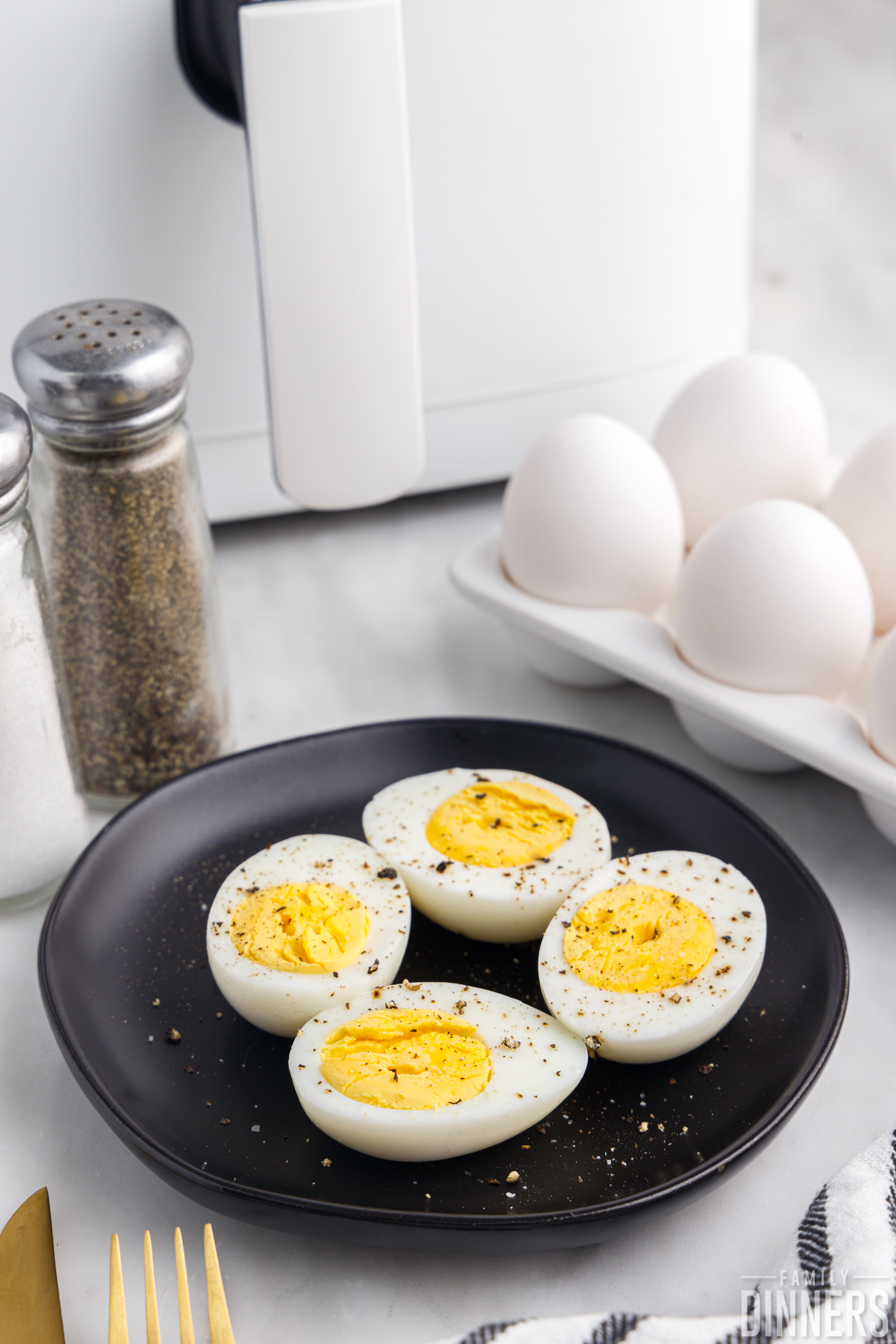 4 eggs sliced open on a black plate in front of air fryer