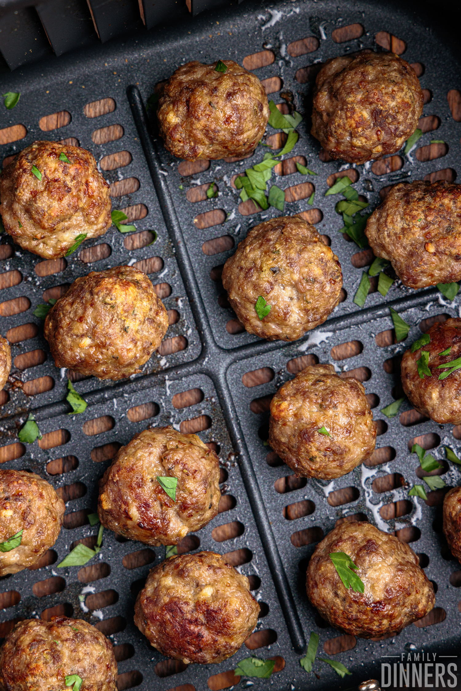 Close-up of cooked meatballs in air fryer basket, sprinkled with chopped parsley. 