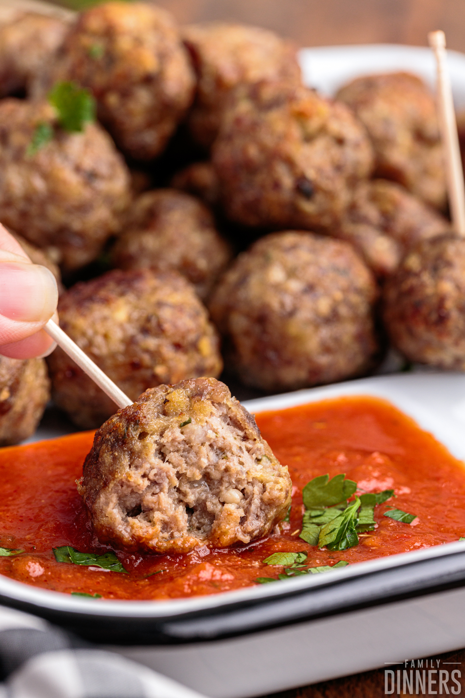 Close up of meatball held by a toothpick being dipped into marinara sauce.