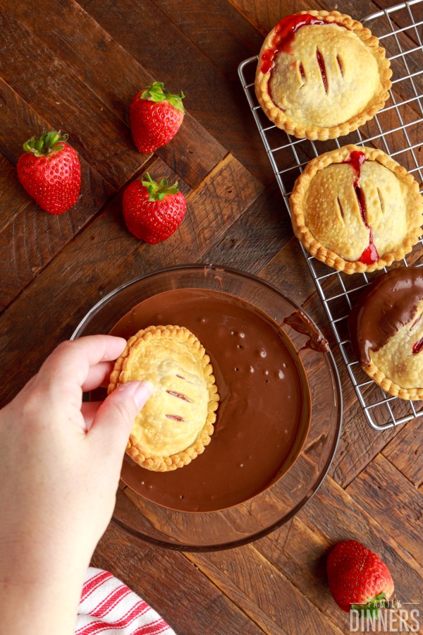 hand dipping strawberry hand pie in melted chocolate