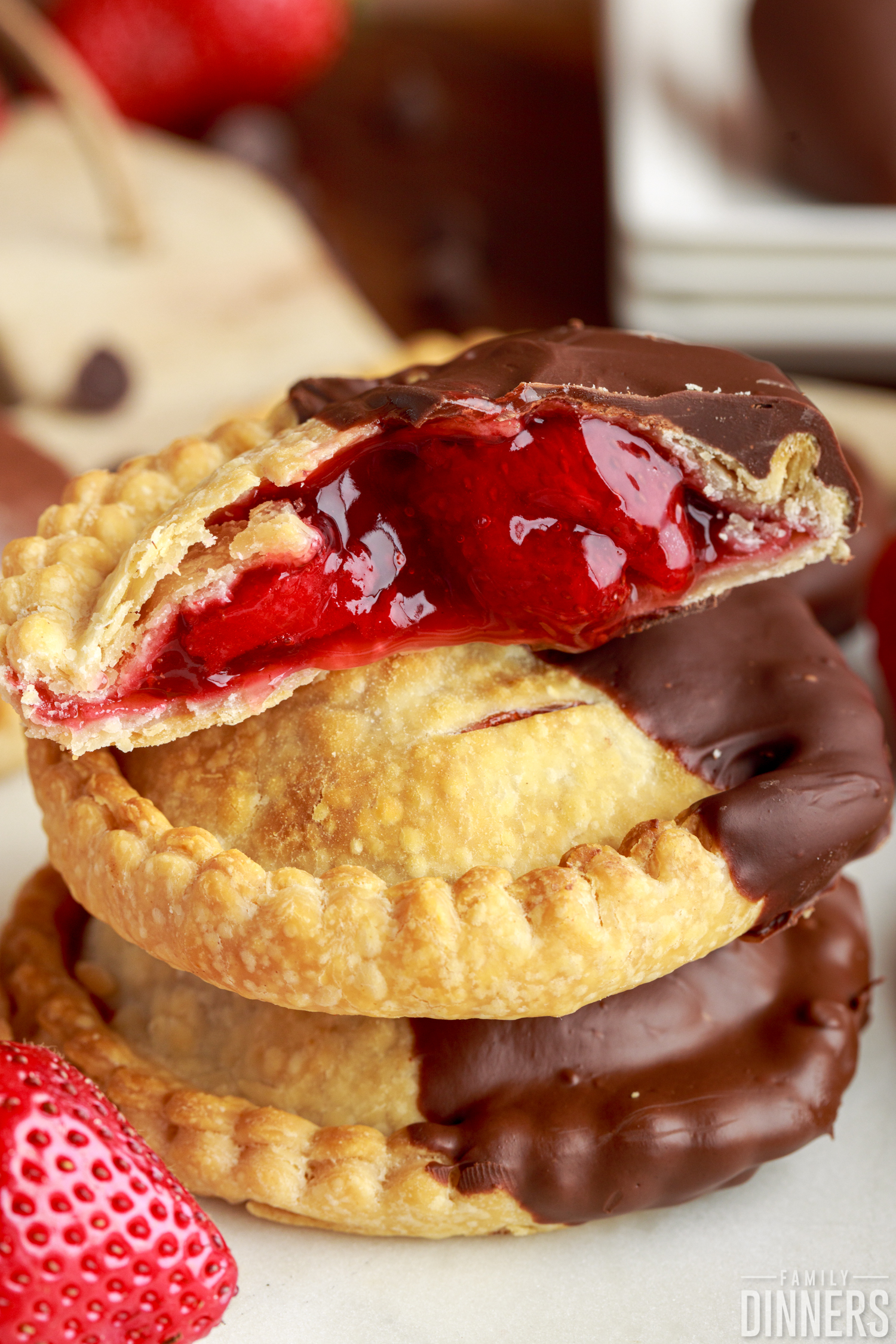hand pies dipped in chocolate stacked on each other, with the top one oozing strawberry filling