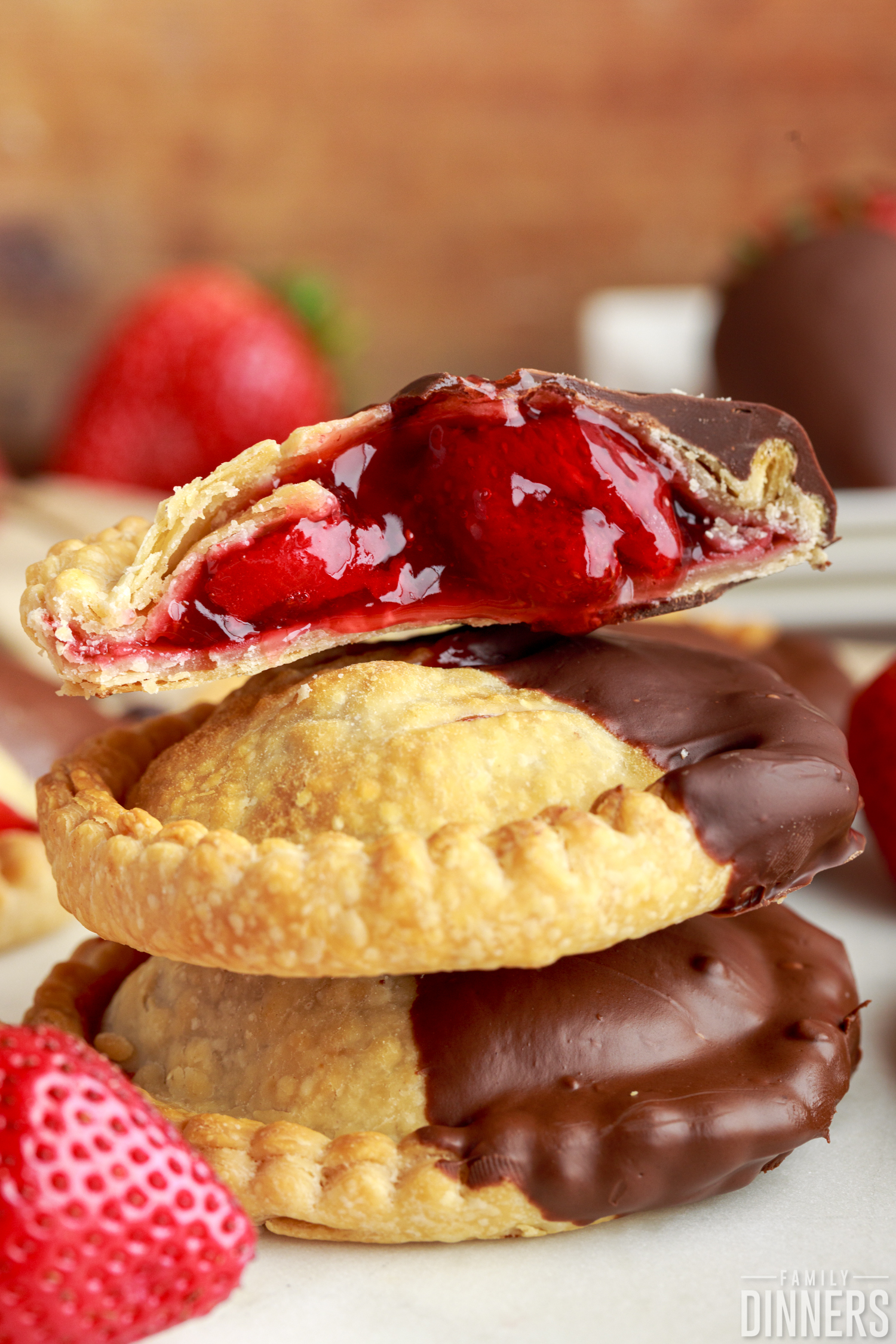 a stack of three chocolate dipped strawberry hand pies with the top one cut in half