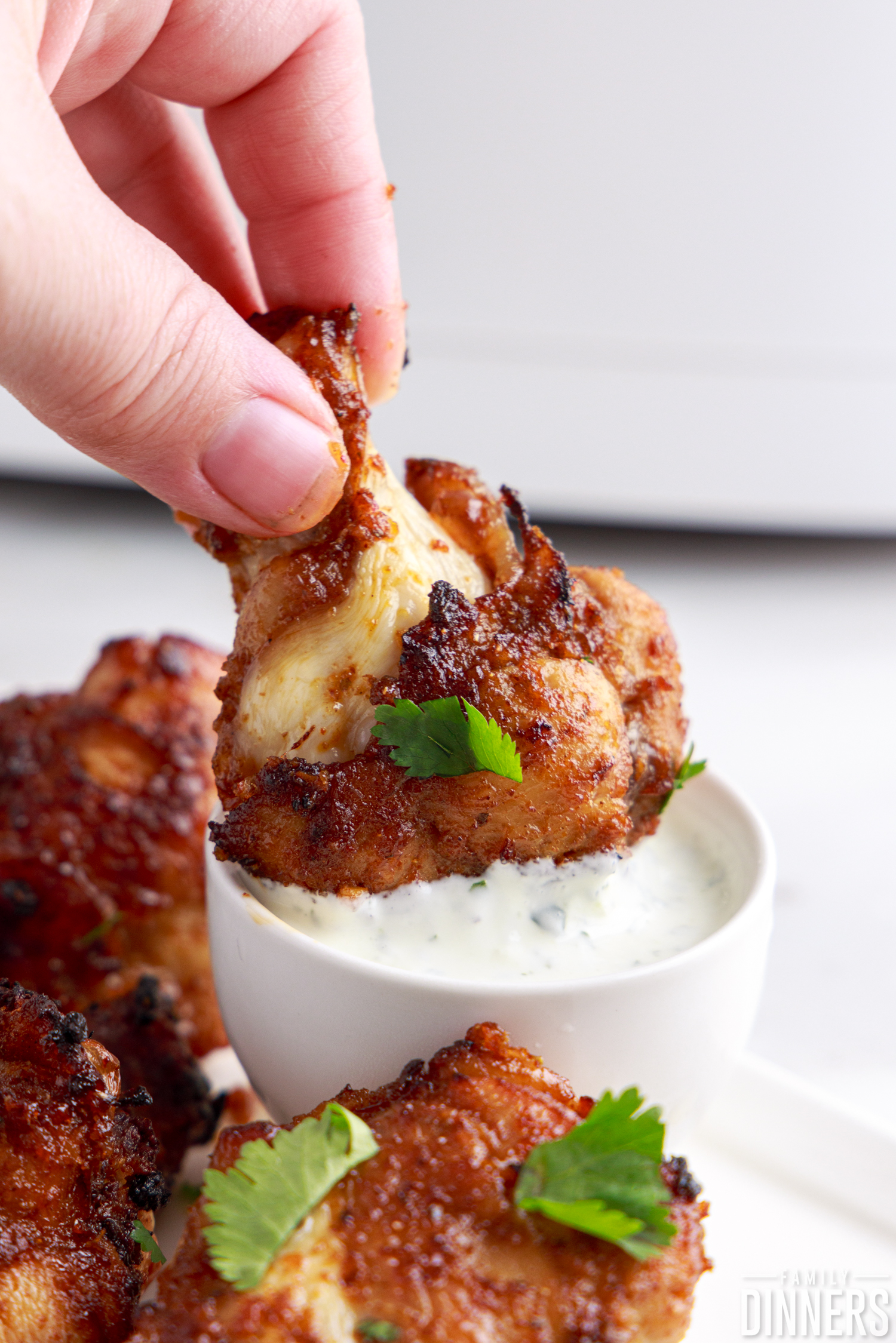 chicken wing being dipped into sour cream sauce with cilantro and lime