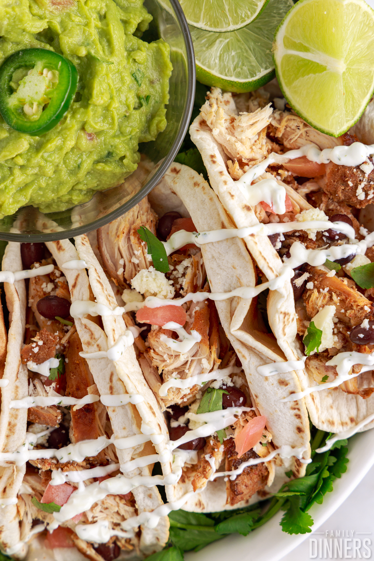 chipotle chicken in flour tortillas drizzled with lime sour cream next to guacamole