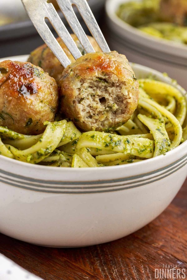 Bowl of pesto fettuccine with a meatball with a bite out on top.